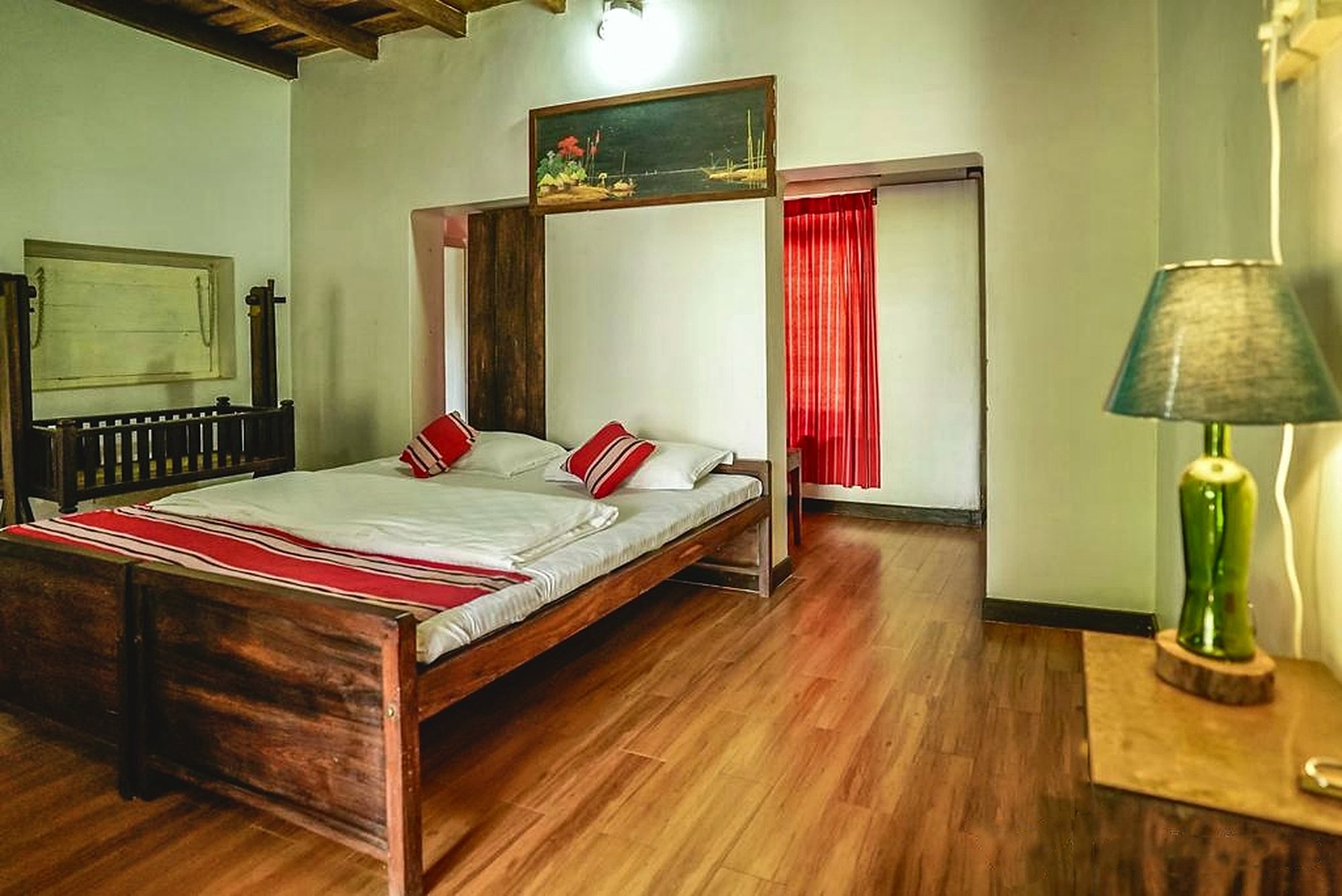 Heavy wooden beds, an antique wooden cradle and a framed riverbank painting beneath timber ceiling beams